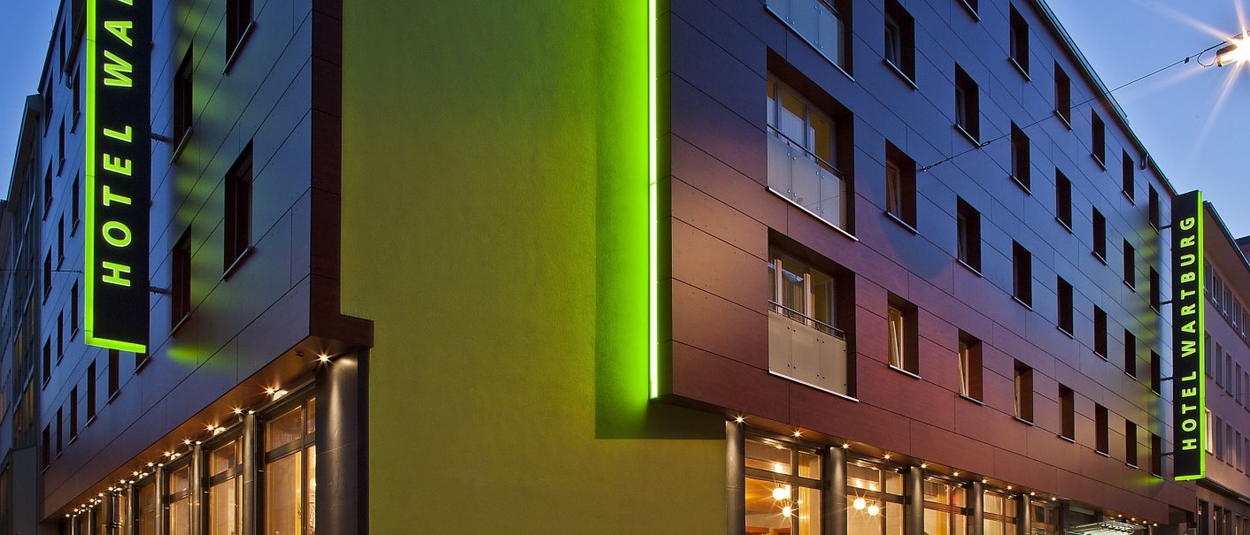 Modern hotel exterior view at dusk, with green lighting and parked cars. The lettering 'Hotel Wartburg' is visible., &copy; VCH Hotel Wartburg