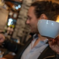 Zwei Personen in einem Caf&eacute;. Eine Person trinkt aus einer Tasse, w&auml;hrend die andere Kaffee zubereitet. Im Hintergrund sind Regale mit Flaschen zu sehen., &copy; Stuttgart Marketing  GmbH, Fotografin Martina Denker