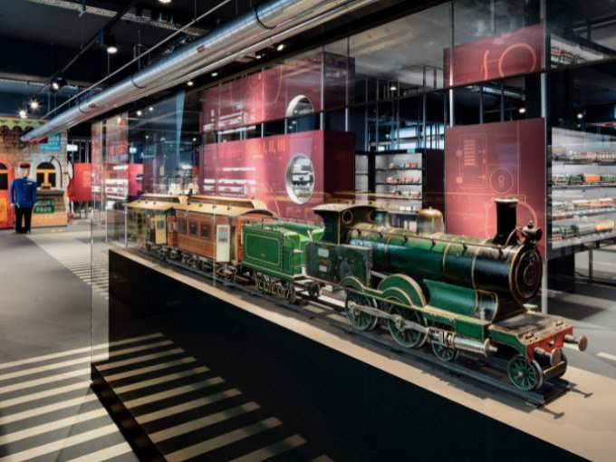 Historical model trains in a glass display case in the Märklineum. Further exhibits and information boards can be seen in the background., © Märklin Spielwaren Vertriebs-GmbH Historical model trains in a glass display case in the Märklineum. Further exhibits and information boards can be seen in the background., © Märklin Spielwaren Vertriebs-GmbH