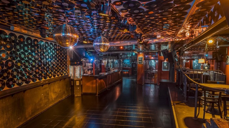 Club mit Schallplatten an Wänden und Decke, Discokugeln und Bar. Stimmungsvolle Beleuchtung und leere Tanzfläche., © Goldmarks, Stuttgart