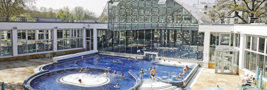 Das SoleBad Bad Cannstatt zeigt ein modernes Schwimmbecken mit Glasfassade. Menschen entspannen im Wasser und auf Liegest&uuml;hlen., &copy; Stuttgarter B&auml;der