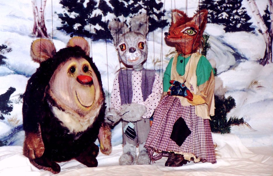 Drei Puppenfiguren, ein Bär, ein Hase und ein Fuchs, sitzen vor einem winterlichen Hintergrund mit Schnee und Bäumen., © Nellys Puppentheater Drei Puppenfiguren, ein Bär, ein Hase und ein Fuchs, sitzen vor einem winterlichen Hintergrund mit Schnee und Bäumen., © Nellys Puppentheater