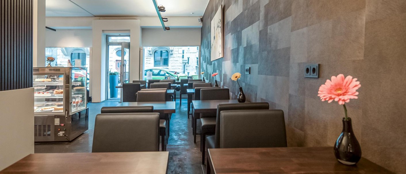 Modern caf&eacute; with dark tables and chairs, vases of flowers on the tables and a cake display case in the background., &copy; Caf&eacute; LIST, Stuttgart