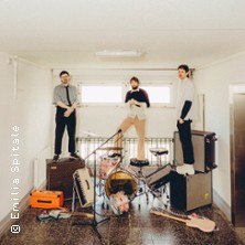 Drei Personen stehen auf Musikinstrumenten in einem kleinen, hellen Raum. Gitarren, Verstärker und ein Schlagzeug sind zu sehen., © links im Bild Drei Personen stehen auf Musikinstrumenten in einem kleinen, hellen Raum. Gitarren, Verstärker und ein Schlagzeug sind zu sehen., © links im Bild