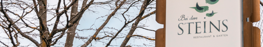 A sign for the restaurant 'Bei den Steins' with birds as a logo, in front of a bare tree and blue sky., © Stuttgart-Marketing GmbH, Sarah Schmid A sign for the restaurant 'Bei den Steins' with birds as a logo, in front of a bare tree and blue sky., © Stuttgart-Marketing GmbH, Sarah Schmid