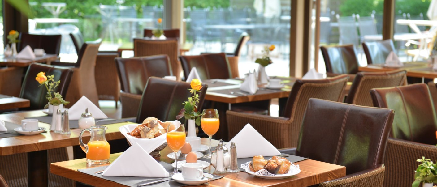 A breakfast table in a conservatory with bread rolls, orange juice and flowers, surrounded by green nature., © Schlosshotel Monrepos A breakfast table in a conservatory with bread rolls, orange juice and flowers, surrounded by green nature., © Schlosshotel Monrepos