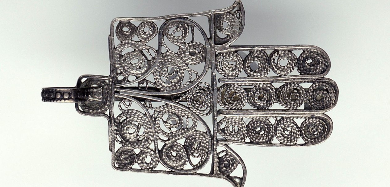 Ein silbernes Hamsa-Amulett mit filigranen, spiralf&ouml;rmigen Mustern. Es symbolisiert Schutz und Gl&uuml;ck., &copy; Linden-Museum Stuttgart
