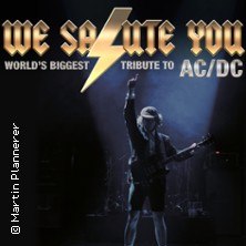 Poster einer Tribute-Band mit Gitarrist im Rampenlicht. Text: "WE SALUTE YOU - World's Biggest Tribute to AC/DC"., &copy; links im Bild