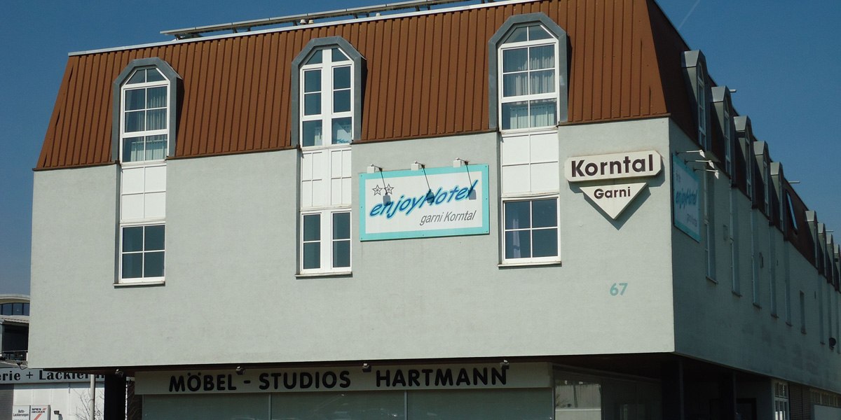 Ein Gebäude mit Schildern von enjoyHotel garni Korntal und Möbel-Studios Hartmann. Das Dach ist braun, die Fassade grau., © enjoyHotel garni Korntal Stuttgart Ein Gebäude mit Schildern von enjoyHotel garni Korntal und Möbel-Studios Hartmann. Das Dach ist braun, die Fassade grau., © enjoyHotel garni Korntal Stuttgart