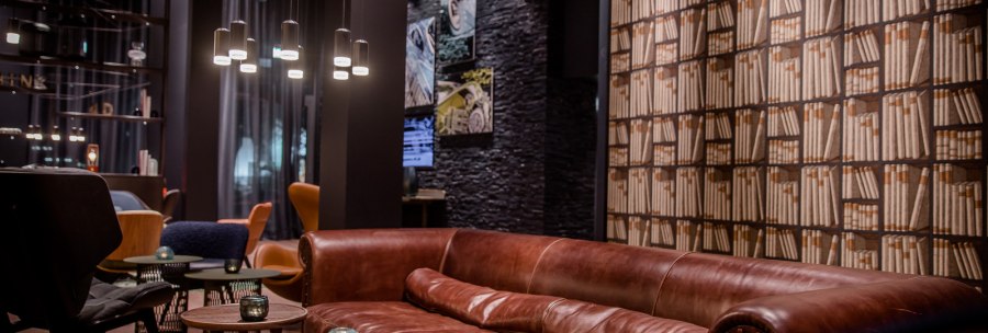 Eleganter Lounge-Bereich mit braunem Ledersofa, runden Holztischen und Bücherregal-Tapete. Moderne Beleuchtung und gemütliche Atmosphäre., © TOMAS Eleganter Lounge-Bereich mit braunem Ledersofa, runden Holztischen und Bücherregal-Tapete. Moderne Beleuchtung und gemütliche Atmosphäre., © TOMAS