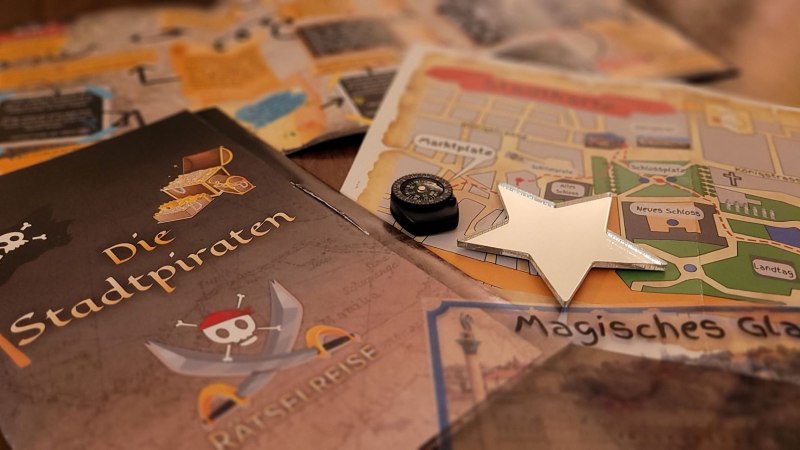 Ein Brettspiel mit dem Titel 'Die Stadtpiraten', Karten, ein Kompass und ein Stern liegen auf einem Tisch. Es scheint ein Rätselspiel zu sein., © SMG