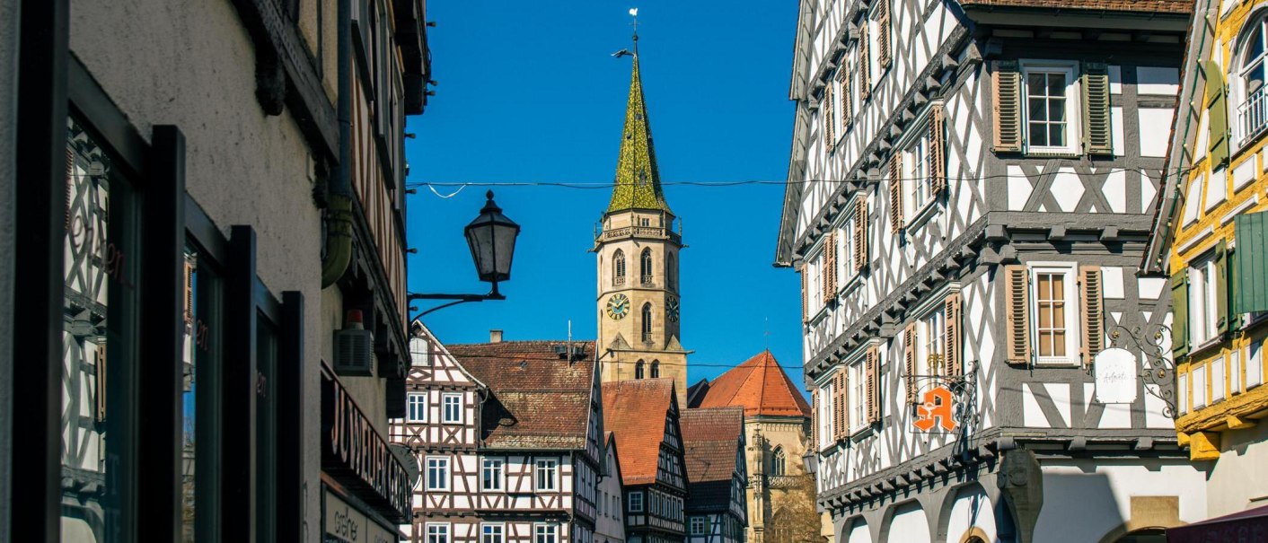Half-timbered houses in the old town of Schorndorf, with a church tower in the background under a clear blue sky., © Stuttgart-Marketing GmbH, Sarah Schmid Half-timbered houses in the old town of Schorndorf, with a church tower in the background under a clear blue sky., © Stuttgart-Marketing GmbH, Sarah Schmid