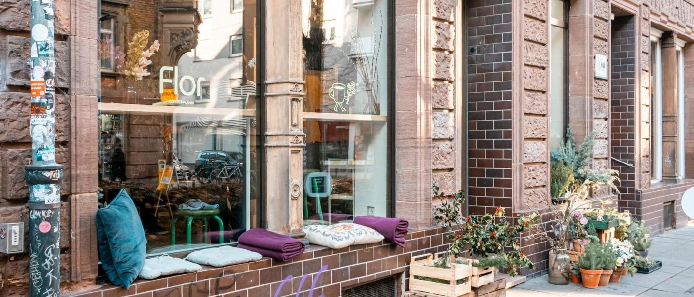Ein gem&uuml;tliches Caf&eacute; mit Pflanzen und Sitzkissen vor dem Fenster. Die Fassade ist aus Backstein, und es gibt Blumenarrangements auf dem Gehweg., &copy; Stuttgart-Marketing GmbH, Sarah Schmid