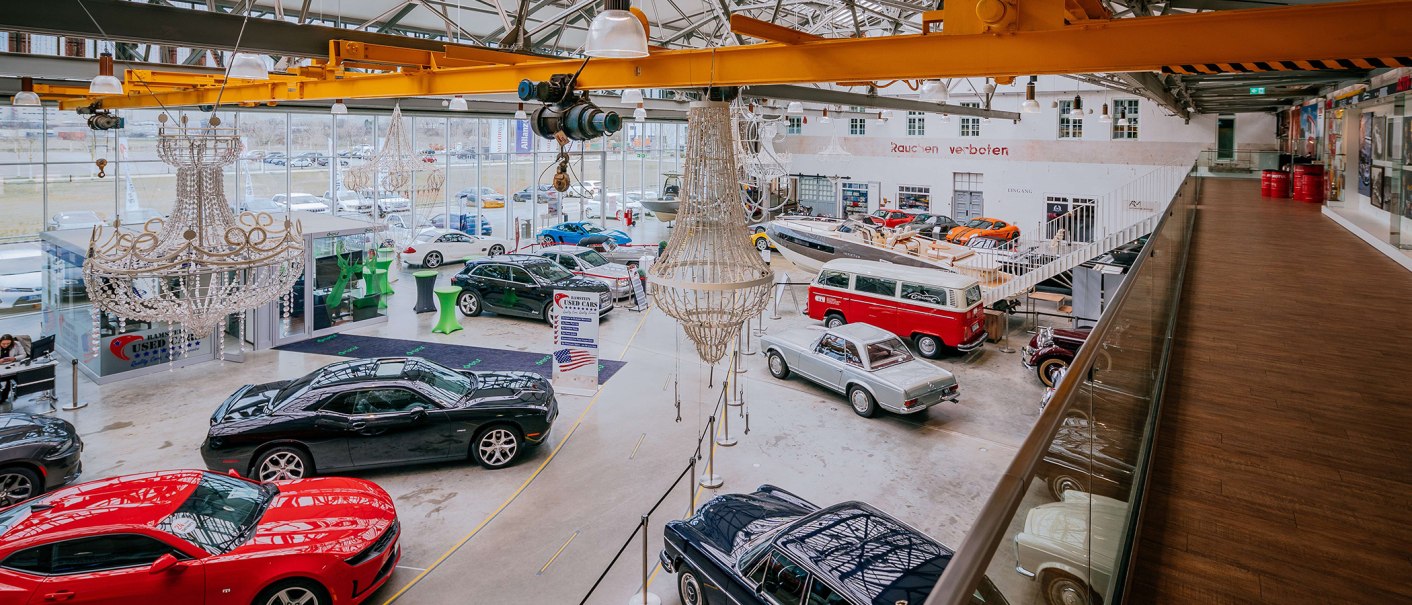 Innenansicht der Motorworld Region Stuttgart mit klassischen Autos, modernen Fahrzeugen und Kronleuchtern in einer großen Halle., © Stuttgart-Marketing GmbH, Thomas Niedermüller