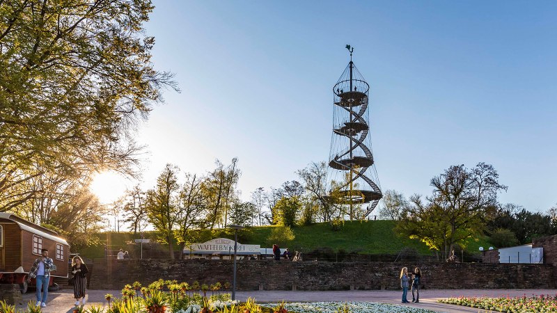 Der Killesbergturm steht in einem Park, umgeben von B&auml;umen. Menschen spazieren bei Sonnenuntergang. Ein Waffelstand ist sichtbar., &copy; Stuttgart-Marketing GmbH, Werner Dieterich