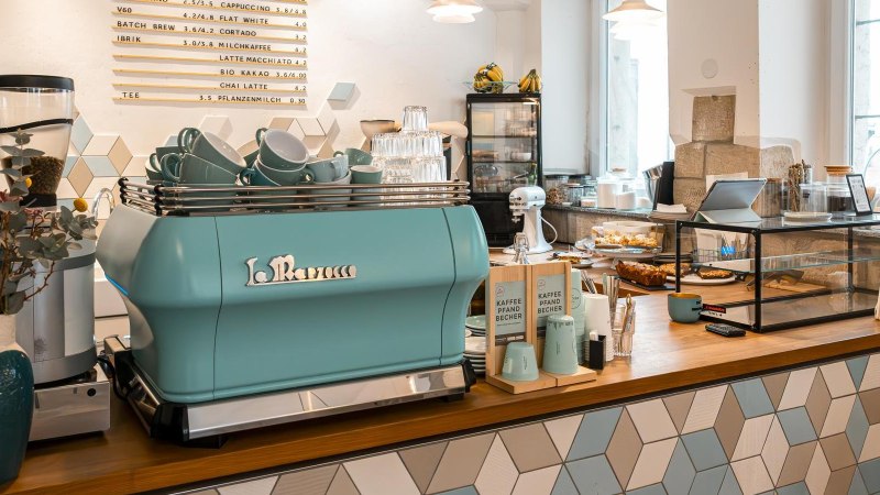 Modernes Café mit blauer Kaffeemaschine, dekorativen Fliesen und Backwaren. Helle, einladende Atmosphäre mit Pflanzen und Zeitschriften., © Stuttgart-Marketing GmbH, Sarah Schmid Modernes Café mit blauer Kaffeemaschine, dekorativen Fliesen und Backwaren. Helle, einladende Atmosphäre mit Pflanzen und Zeitschriften., © Stuttgart-Marketing GmbH, Sarah Schmid