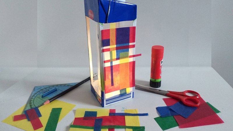 Selbstgemachte Laterne aus Milchkarton mit buntem Transparentpapier, umgeben von Schere, Kleber und Geodreieck auf einem Tisch., © StadtPalais Selbstgemachte Laterne aus Milchkarton mit buntem Transparentpapier, umgeben von Schere, Kleber und Geodreieck auf einem Tisch., © StadtPalais