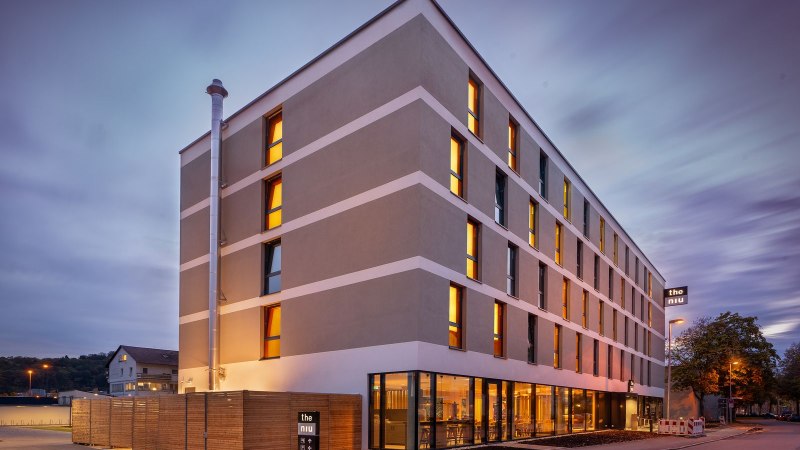 Moderne Hotelaußenfassade bei Dämmerung, beleuchtete Fenster, Schild mit 'the niu'., © Novum Hospitality