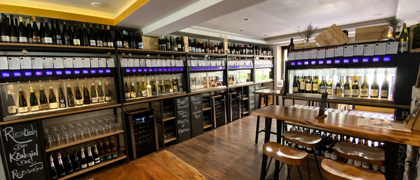 Weinladen mit Regalen voller Weinflaschen, Verkostungstischen und Gläsern. Moderne Einrichtung mit Holz- und Metallelementen., © Sitt-Wein