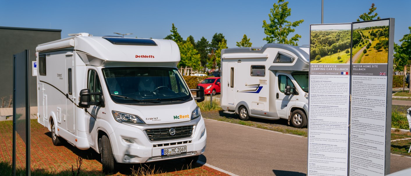 Wohnmobilstellplatz in Fellbach mit mehreren geparkten Wohnmobilen und einer Infotafel. Sonniges Wetter, blauer Himmel und gr&uuml;ne B&auml;ume im Hintergrund., &copy; Stuttgart-Marketing GmbH, Thomas Niederm&uuml;ller