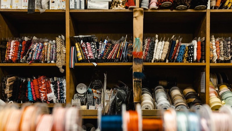 Ein Regal voller bunter Bänder und Garnrollen in einem Nähgeschäft. Verschiedene Farben und Muster sind ordentlich sortiert., © Stuttgart-Marketing GmbH, Sarah Schmid Ein Regal voller bunter Bänder und Garnrollen in einem Nähgeschäft. Verschiedene Farben und Muster sind ordentlich sortiert., © Stuttgart-Marketing GmbH, Sarah Schmid