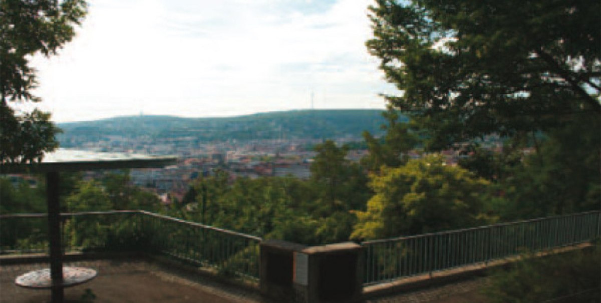 Aussichtsplattform mit Geländer, umgeben von Bäumen, bietet Blick auf eine Stadt und Hügel im Hintergrund., © Stuttgart-Marketing GmbH Aussichtsplattform mit Geländer, umgeben von Bäumen, bietet Blick auf eine Stadt und Hügel im Hintergrund., © Stuttgart-Marketing GmbH