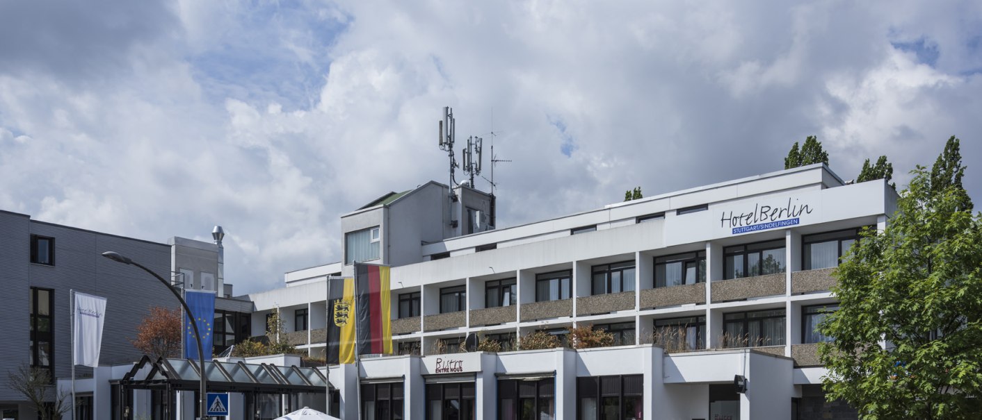 Modernes Hotel mit Flaggen und geparkten Autos, blauer Himmel im Hintergrund., © Hotel Berlin aZIS Hotel BetriebsGmbH