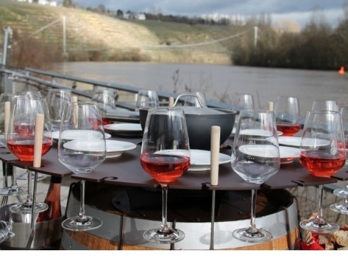 Ein Fass mit Fondue-Set und Weingläsern, gefüllt mit Roséwein, steht im Freien vor einem Fluss und einer Hügellandschaft., © Cool-Tours StattReisen Ein Fass mit Fondue-Set und Weingläsern, gefüllt mit Roséwein, steht im Freien vor einem Fluss und einer Hügellandschaft., © Cool-Tours StattReisen