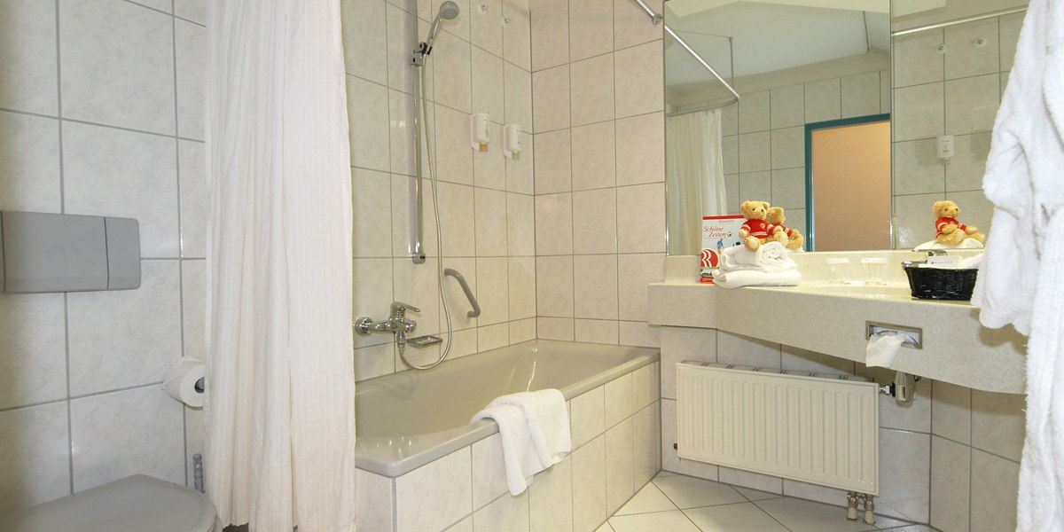 Ein helles Badezimmer mit Badewanne, Duschvorhang, Waschbecken und Spiegel. Handtücher und Dekorationen auf dem Waschbecken., © © H-Hotels.com Ein helles Badezimmer mit Badewanne, Duschvorhang, Waschbecken und Spiegel. Handtücher und Dekorationen auf dem Waschbecken., © © H-Hotels.com