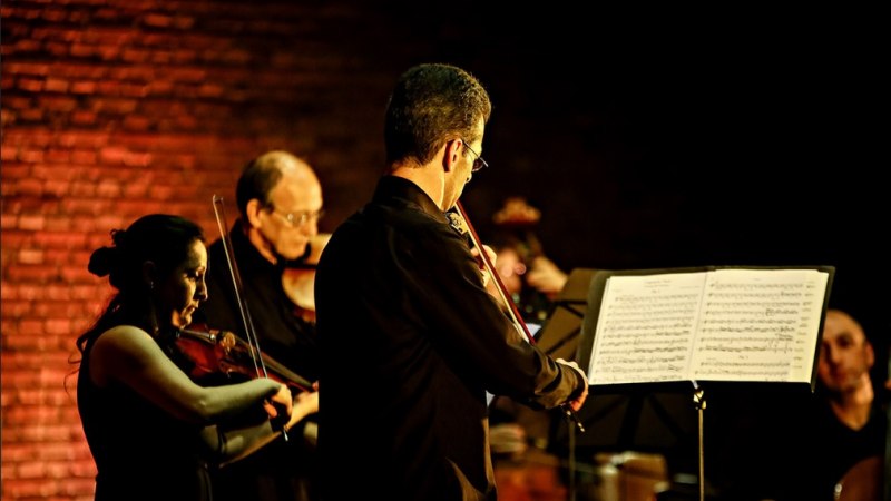 Musiker spielen Streichinstrumente in einem Konzert. Sie stehen vor einem Notenständer, die Bühne ist in warmes Licht getaucht., © Tigran Mikaelyan Musiker spielen Streichinstrumente in einem Konzert. Sie stehen vor einem Notenständer, die Bühne ist in warmes Licht getaucht., © Tigran Mikaelyan