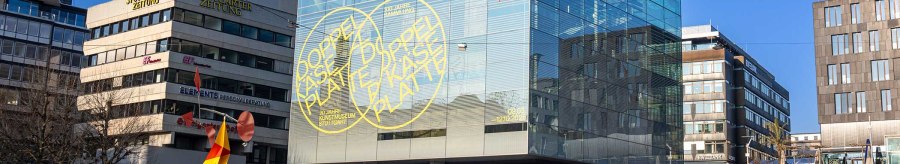 Das Kunstmuseum Stuttgart mit seinem markanten Glaskubus am Schlossplatz. Eine bunte Skulptur steht im Vordergrund, umgeben von modernen Geb&auml;uden., &copy; Stuttgart-Marketing GmbH, Sarah Schmid