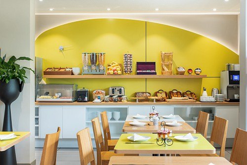 Modern breakfast buffet with bread, fruit, cereals and coffee machine. Bright, friendly atmosphere with wooden tables and green accents., &copy; adagio access Stuttgart Airport Messe