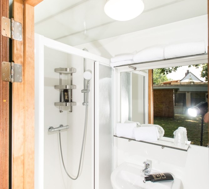 Kompaktes Badezimmer mit Dusche, Waschbecken und Handtüchern. Helle Beleuchtung und Holzdetails. Blick nach draußen durch ein Fenster., © Remsfässer