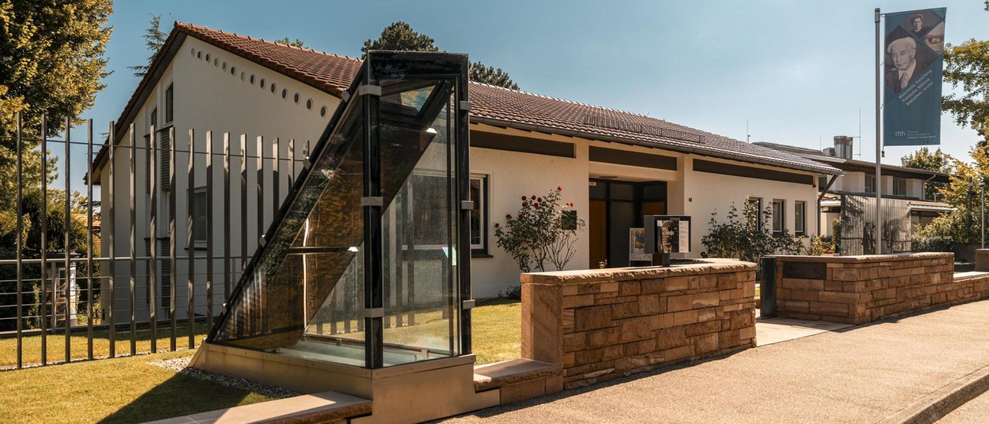 Das Theodor-Heuss-Haus mit moderner Glasfassade und gepflegtem Garten. Ein Banner mit Porträt ist sichtbar. Sonniger Tag mit klarem Himmel., © Stuttgart Marketing GmbH, Sarah Schmid