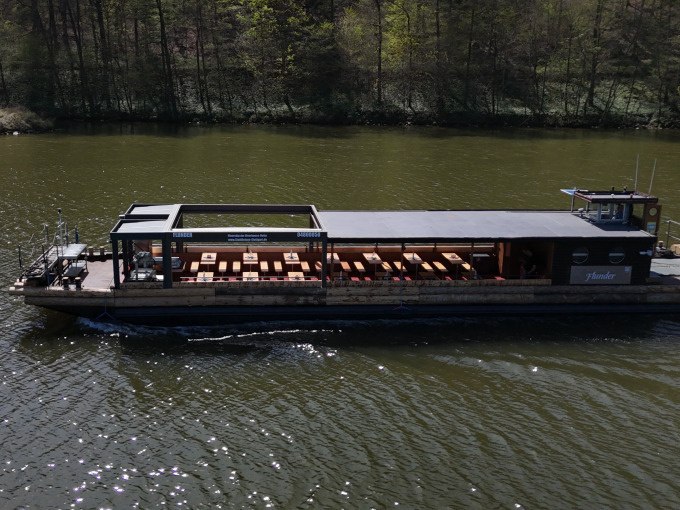 Ein Flussschiff mit überdachten Sitzbänken fährt auf einem ruhigen Fluss, umgeben von bewaldeten Ufern., © Cool-Tours StattReisen Ein Flussschiff mit überdachten Sitzbänken fährt auf einem ruhigen Fluss, umgeben von bewaldeten Ufern., © Cool-Tours StattReisen