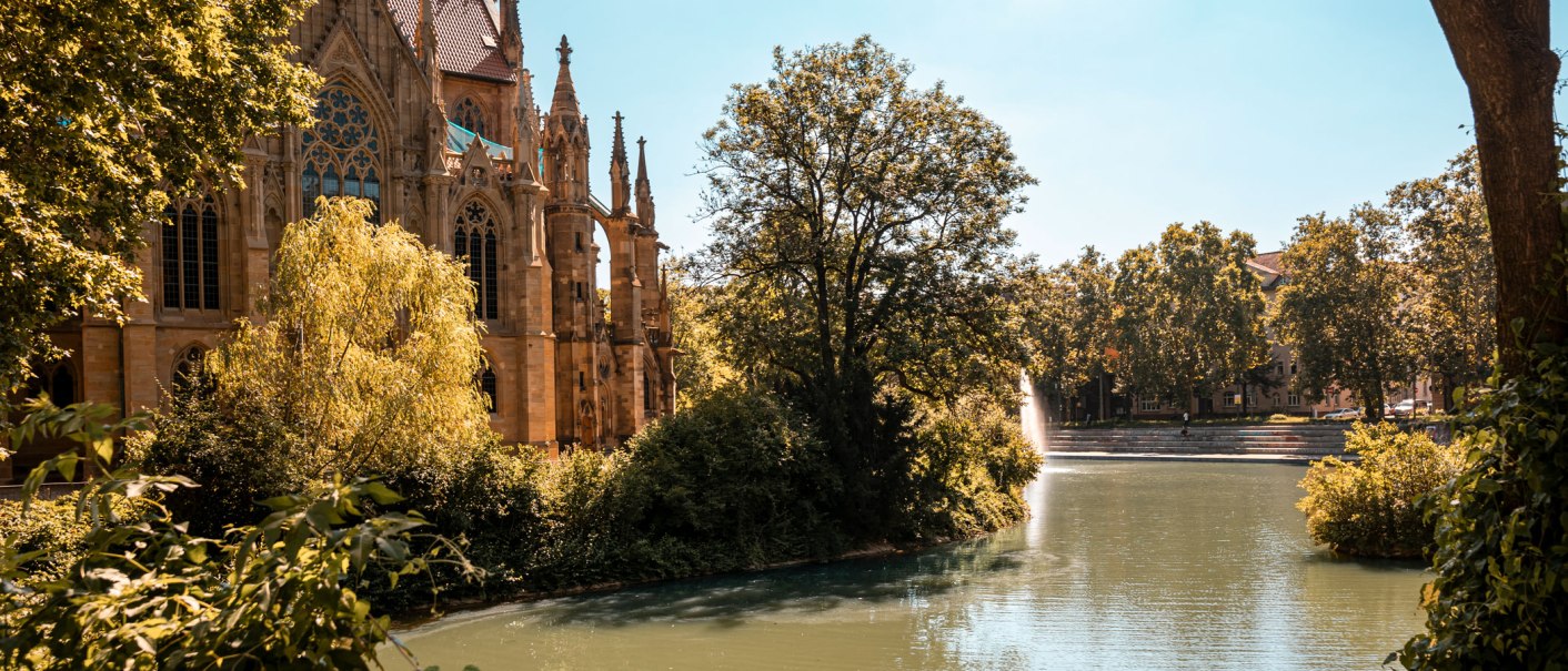 Die Johanneskirche am Feuersee, umgeben von Bäumen und Wasser, bei sonnigem Wetter., © SMG, Sarah Schmid