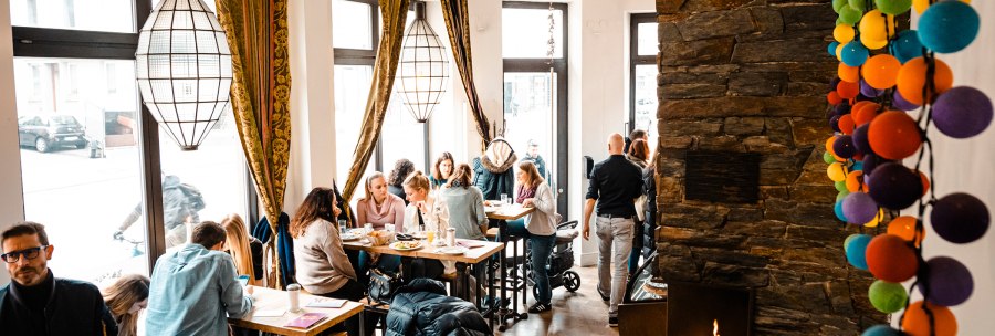 Gem&uuml;tliches Caf&eacute; mit gro&szlig;en Fenstern, Menschen an Tischen, bunte Kugeln an der Wand und ein Kamin. Warme, einladende Atmosph&auml;re., &copy; Stuttgart-Marketing GmbH, Sarah Schmid
