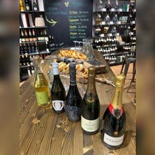 Ein Tisch in einem Weinladen mit Sektflaschen und Brezeln. Im Hintergrund sind Weinregale und eine Tafel mit Angeboten zu sehen., &copy; links im Bild