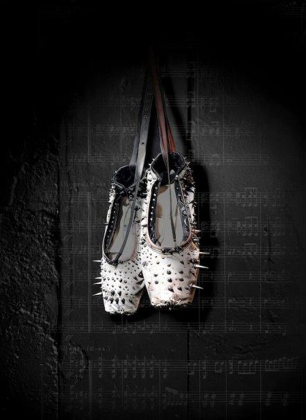 A pair of studded ballet shoes hangs in front of a dark background with sheet music. The shoes combine classic elegance with punk style., &copy; Theaterhaus Stuttgart e.V.