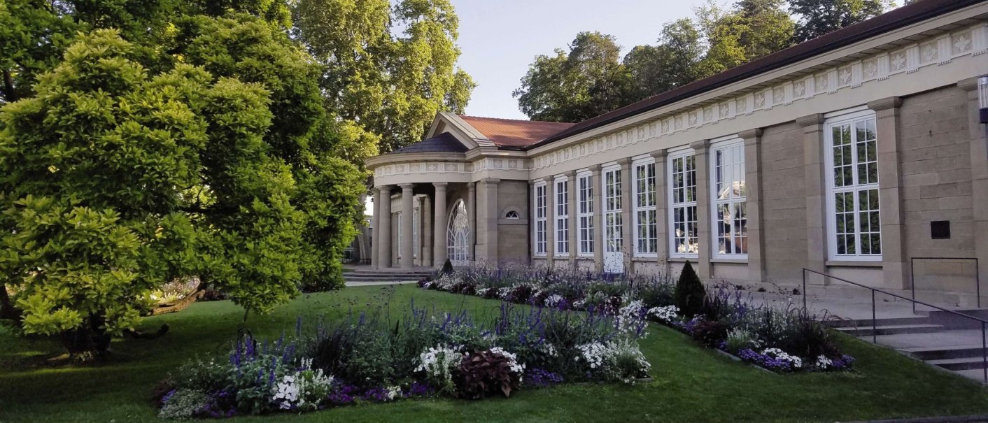 Historisches Gebäude mit Säulen und großen Fenstern, umgeben von gepflegtem Garten und blühenden Blumenbeeten., © Stuttgart-Marketing GmbH Historisches Gebäude mit Säulen und großen Fenstern, umgeben von gepflegtem Garten und blühenden Blumenbeeten., © Stuttgart-Marketing GmbH