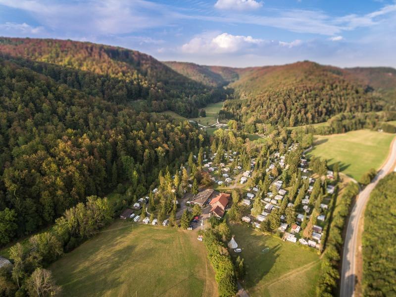 Luftaufnahme des Campingplatzes Pf&auml;hlhof in einem bewaldeten Tal mit Wohnwagen und Zelten, umgeben von H&uuml;geln und einer Stra&szlig;e., &copy; Campingplatz Pf&auml;hlhof
