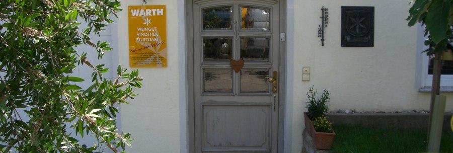Entrance to the Warth winery with yellow sign, plants and wooden door. A thermometer and a coat of arms are attached to the wall., © Weingut Warth