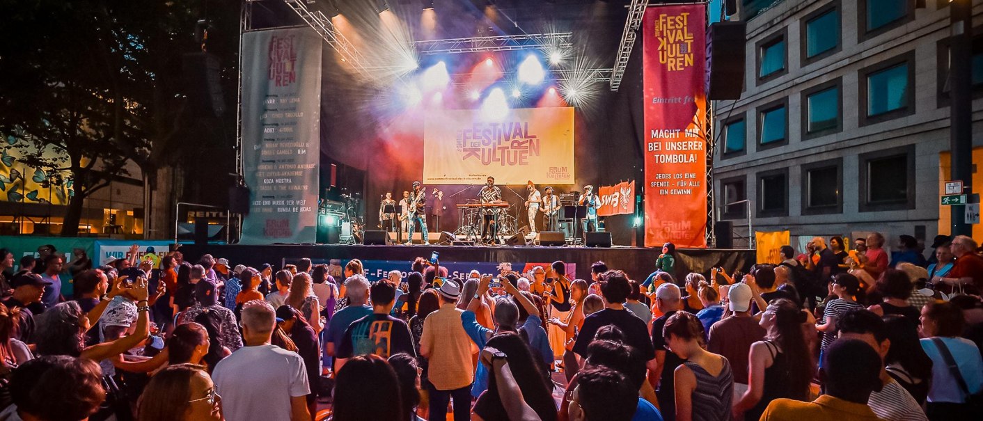 Große Menschenmenge vor einer Bühne beim Sommerfestival der Kulturen. Musiker spielen, bunte Lichter und Banner im Hintergrund., © Forum der Kulturen Stuttgart e. V. Große Menschenmenge vor einer Bühne beim Sommerfestival der Kulturen. Musiker spielen, bunte Lichter und Banner im Hintergrund., © Forum der Kulturen Stuttgart e. V.
