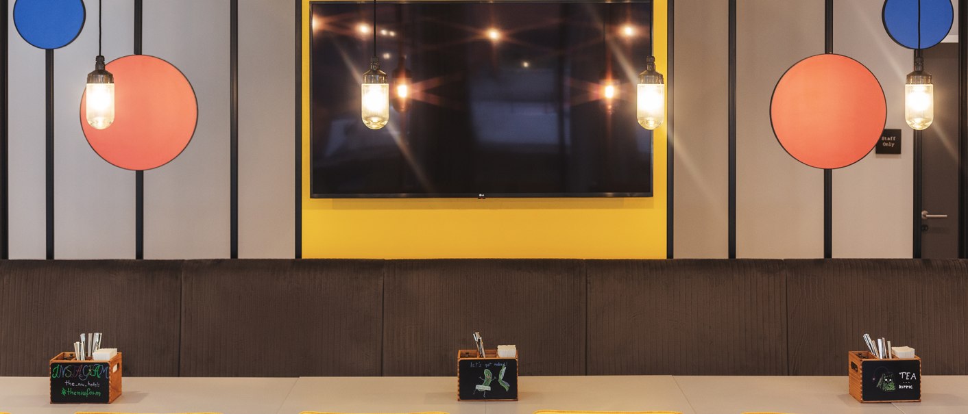 A modern restaurant with colorful circles on the wall, hanging lamps, and tables with cutlery boxes., © the niu Form - Novum Hospitality A modern restaurant with colorful circles on the wall, hanging lamps, and tables with cutlery boxes., © the niu Form - Novum Hospitality