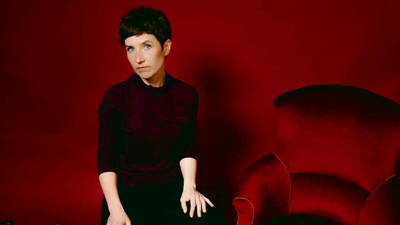 Frau sitzt in einem roten Raum neben einem roten Sessel. Ein Cello und eine Schale mit Erdbeeren sind zu sehen., &copy; Judith Goldbach