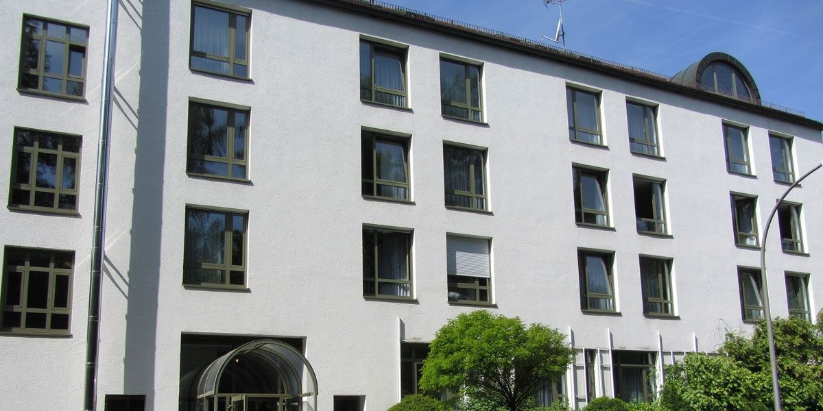 A multi-story building with white walls and numerous windows, surrounded by trees and shrubs., &copy; Christk&ouml;nigshaus