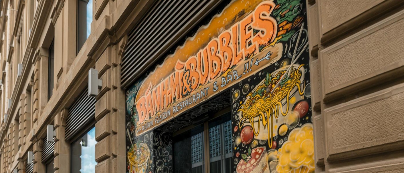 Gebäudefassade mit dem Schild 'Banh Mi & Bubbles' und buntem Wandgemälde mit asiatischen Motiven., © Stuttgart-Marketing GmbH, Sarah Schmid
