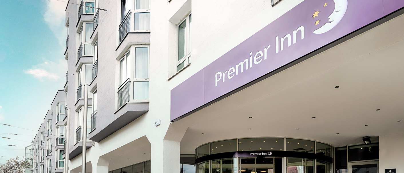 Au&szlig;enansicht eines Premier Inn Hotels mit lila Schild und Eingangst&uuml;r. Mehrst&ouml;ckiges Geb&auml;ude mit gro&szlig;en Fenstern., &copy; Premier Inn Germany