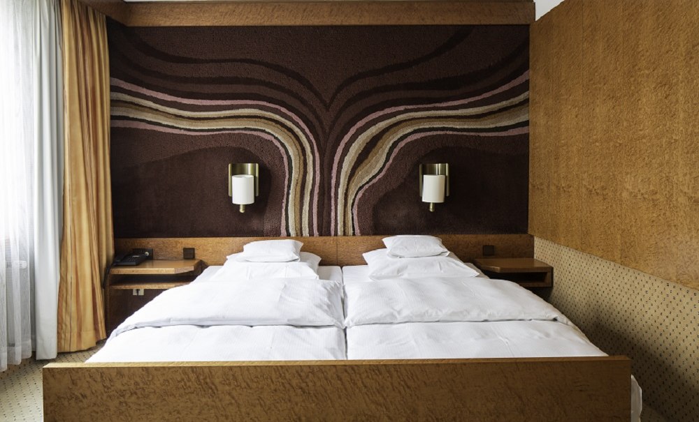 Doppelzimmer mit zwei Einzelbetten, brauner Wandteppich mit Wellenmuster, orange Vorhänge und helle Bettwäsche., © Hotel Royal