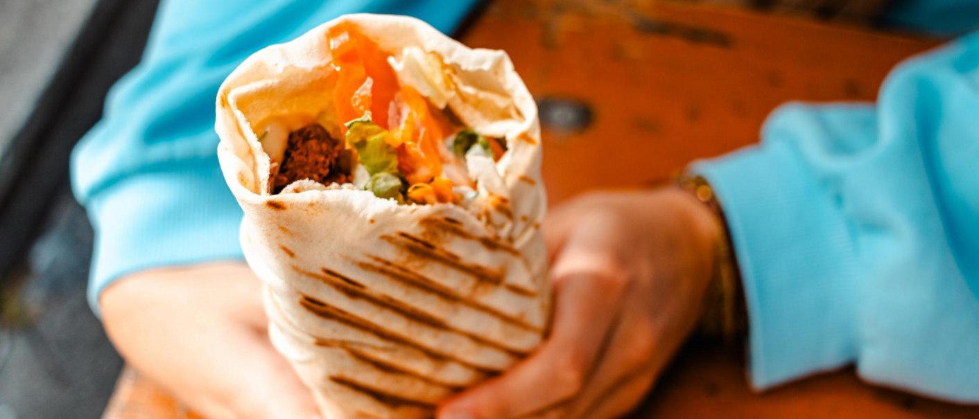 Ein gefüllter Wrap mit Gemüse und Falafel wird von einer Person in blauer Kleidung gehalten., © Stuttgart-Marketing GmbH, Sarah Schmid